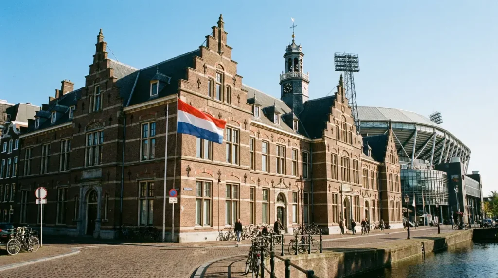 Edificio institucional holandés con bandera de los Países Bajos ondeando junto a un estadio de fútbol